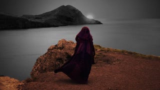 The Acolyte stands looking over a sandy sea, with the background in black and white and the foreground in colour.